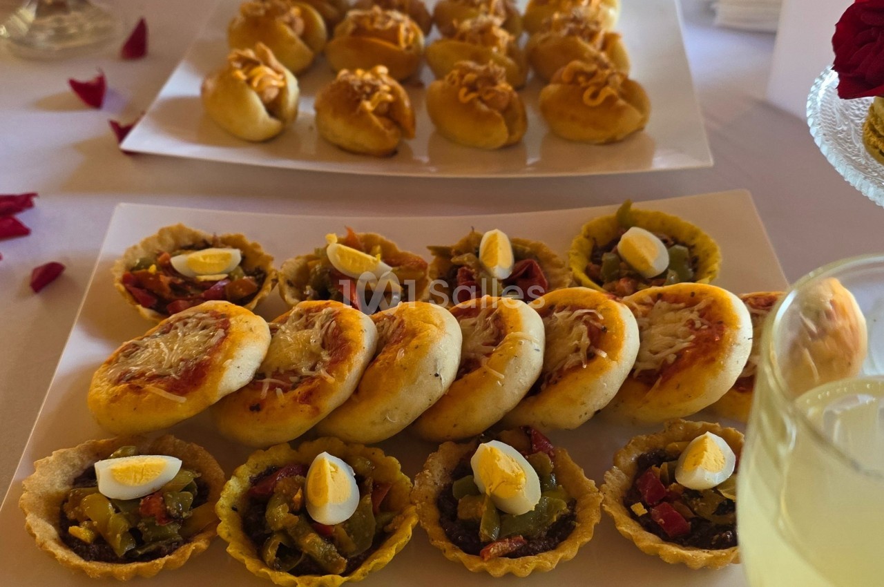 Assortiment de mini-tartelettes garnies de légumes et œufs, accompagné de petits pains salés sur une table.