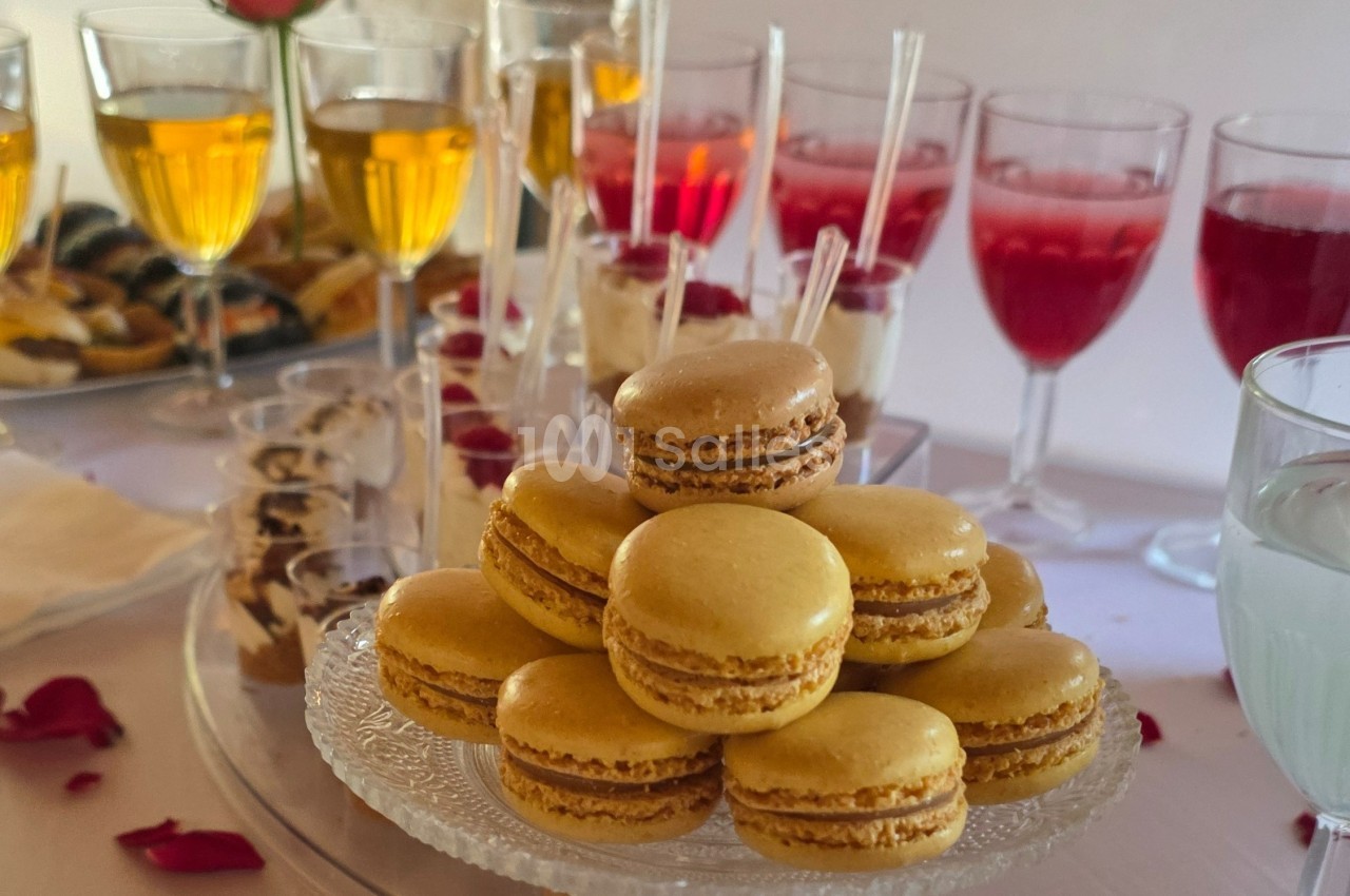 Plateau de macarons dorés sur une table de réception avec verrines et boissons en arrière-plan.