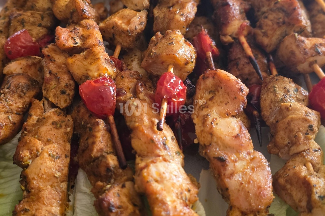 Brochettes de poulet grillé assaisonnées, accompagnées de morceaux de poivrons rouges, servies sur un lit de salade.