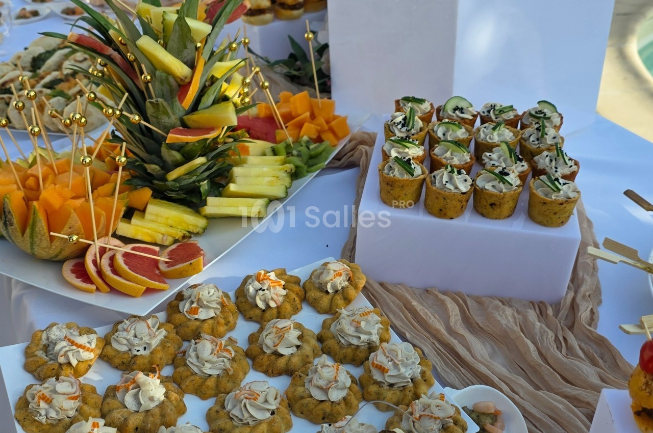 Plateau de buffet avec fruits frais, verrines garnies et petits amuse-bouches disposés sur une table blanche.