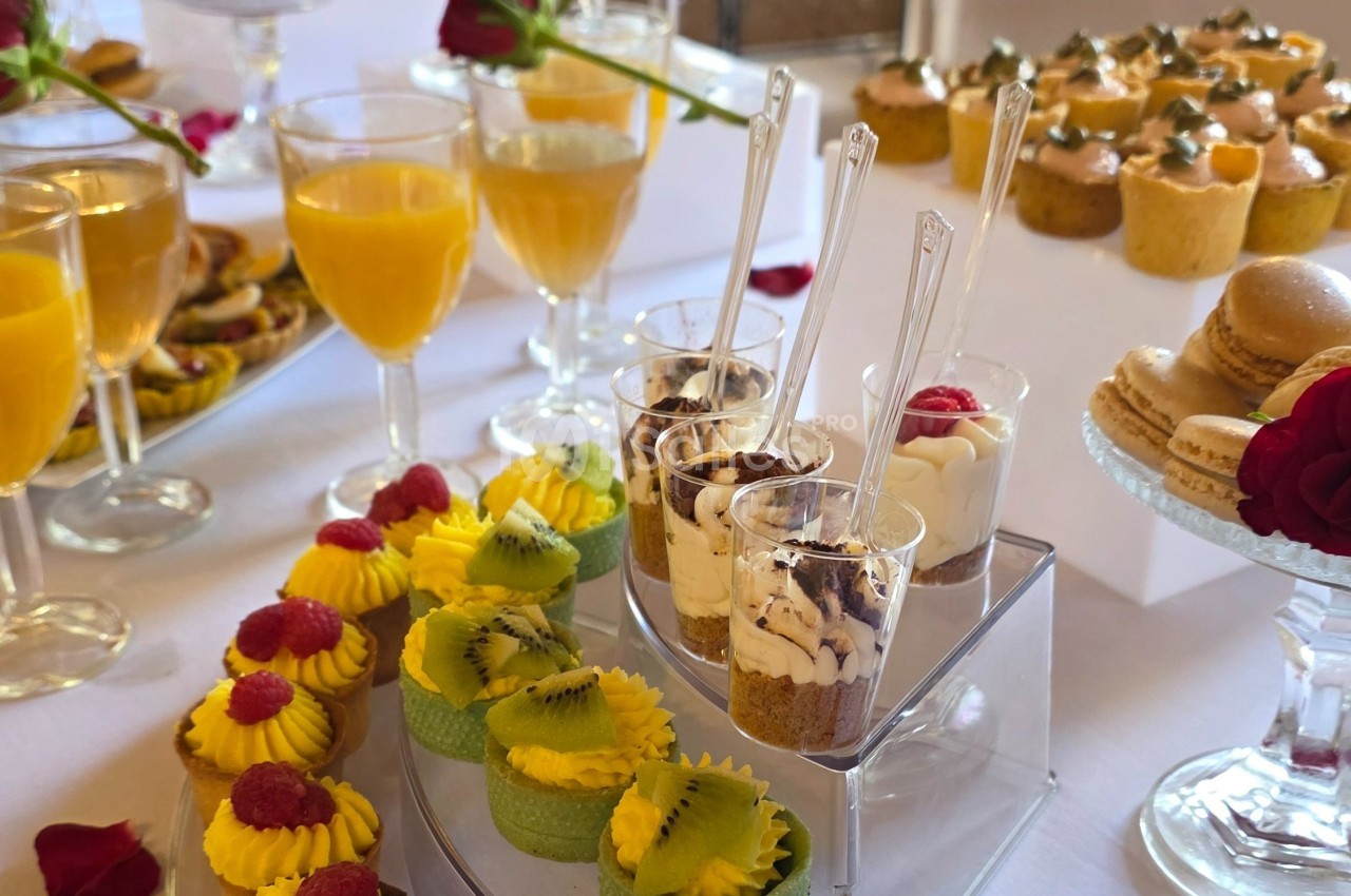 Desserts variés présentés sur une table, incluant verrines, macarons, pâtisseries aux fruits et verres de jus d'orange.