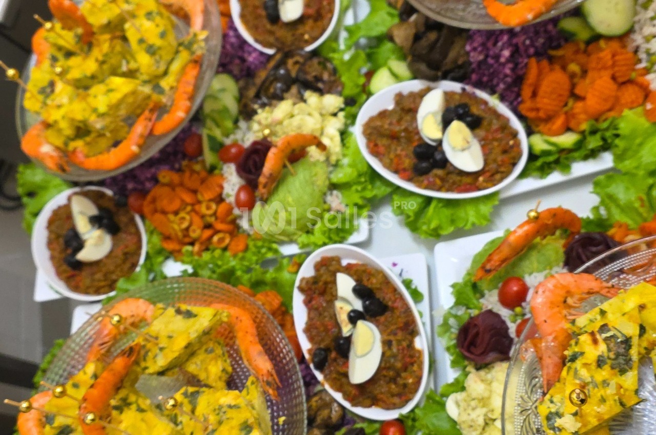 Plats variés composés de salades, crevettes, œufs, olives et légumes, présentés sur une table garnie de verdure.