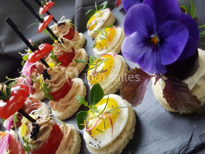 Assortiment de canapés colorés garnis de légumes, fleurs comestibles et herbes fraîches sur un plateau.