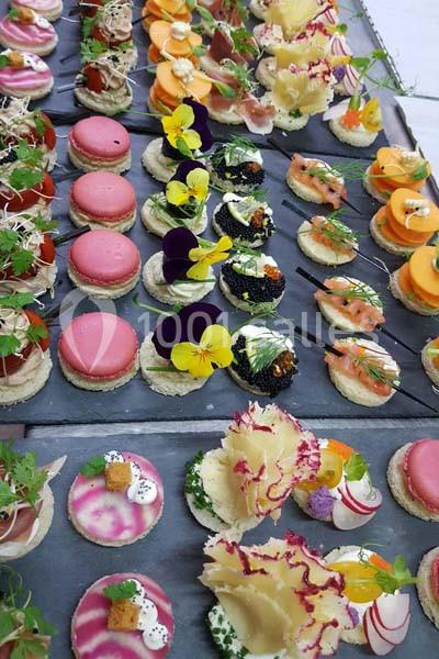 Plateau de canapés variés avec des garnitures colorées, incluant fleurs comestibles, légumes et macarons salés.