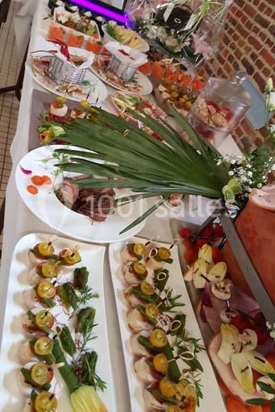 Buffet varié avec plats froids, brochettes de légumes, viandes et décorations florales sur une table blanche.