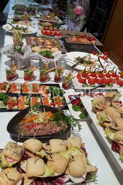 Buffet varié composé de mini-sandwichs, verrines, brochettes et plats garnis, présenté sur une grande table.