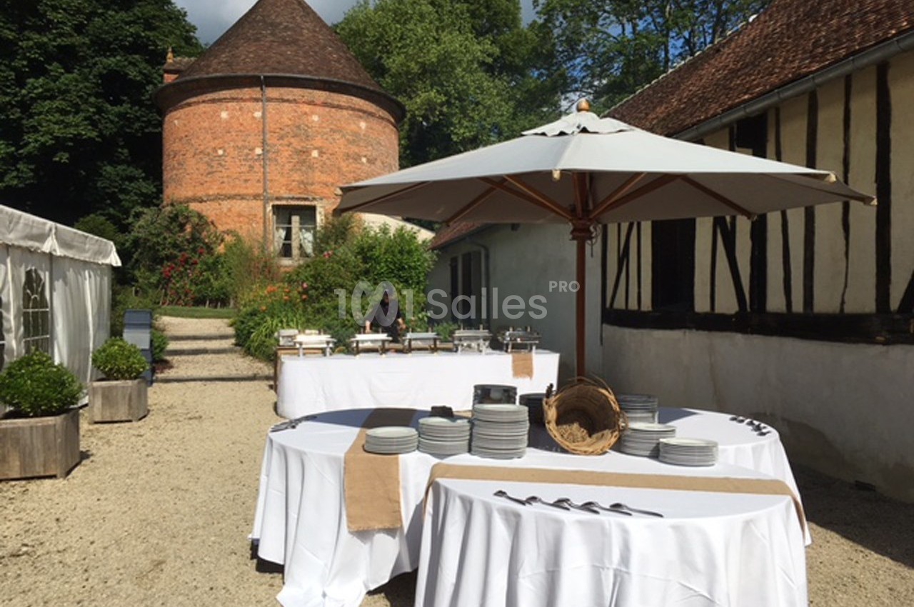 Tables dressées en extérieur avec vaisselle et couverts, près d'un bâtiment à colombages et d'une tour en briques.