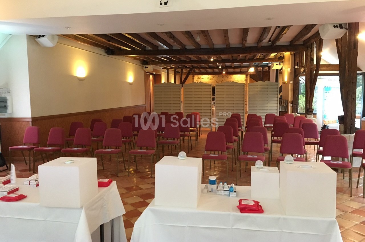 Salle de réunion avec des rangées de chaises rouges alignées, tables blanches au premier plan et cloisons au fond.