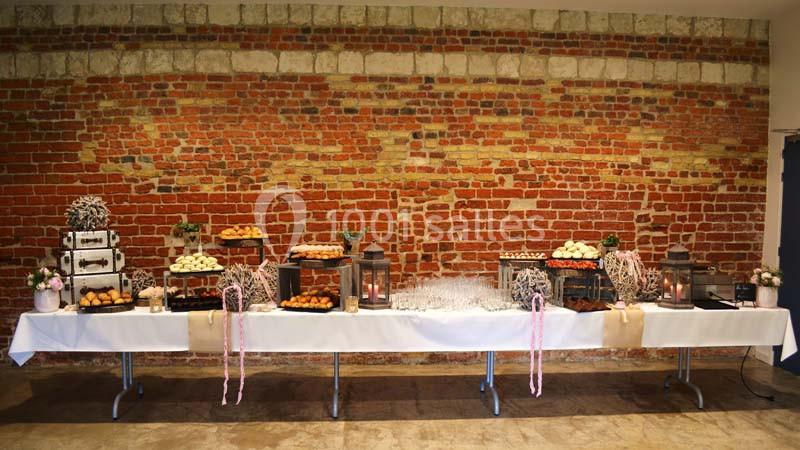 Table dressée avec des desserts variés, lanternes décoratives et éléments floraux, devant un mur de briques rouges.