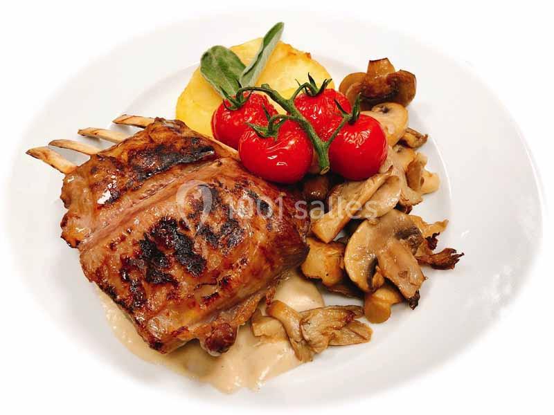 Carré d'agneau grillé accompagné de champignons, tomates cerises rôties et purée, servi sur une assiette blanche.