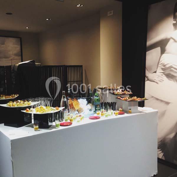 Table de buffet avec verrines, amuse-bouches, bouteilles d'eau et décor sobre en arrière-plan.