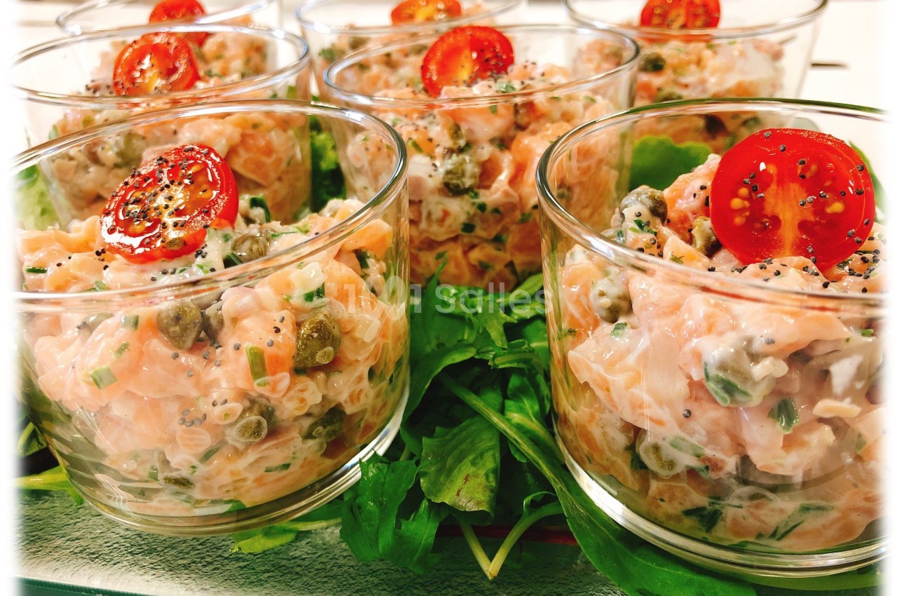 Verrines de tartare de saumon avec câpres, herbes fraîches et rondelles de tomate cerise sur lit de roquette.