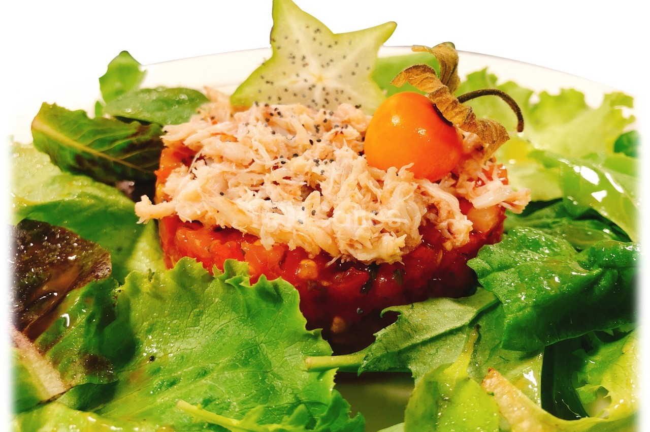 Tartare de tomates sur lit de salade verte, garni de chair de crabe, physalis et étoile de carambole.