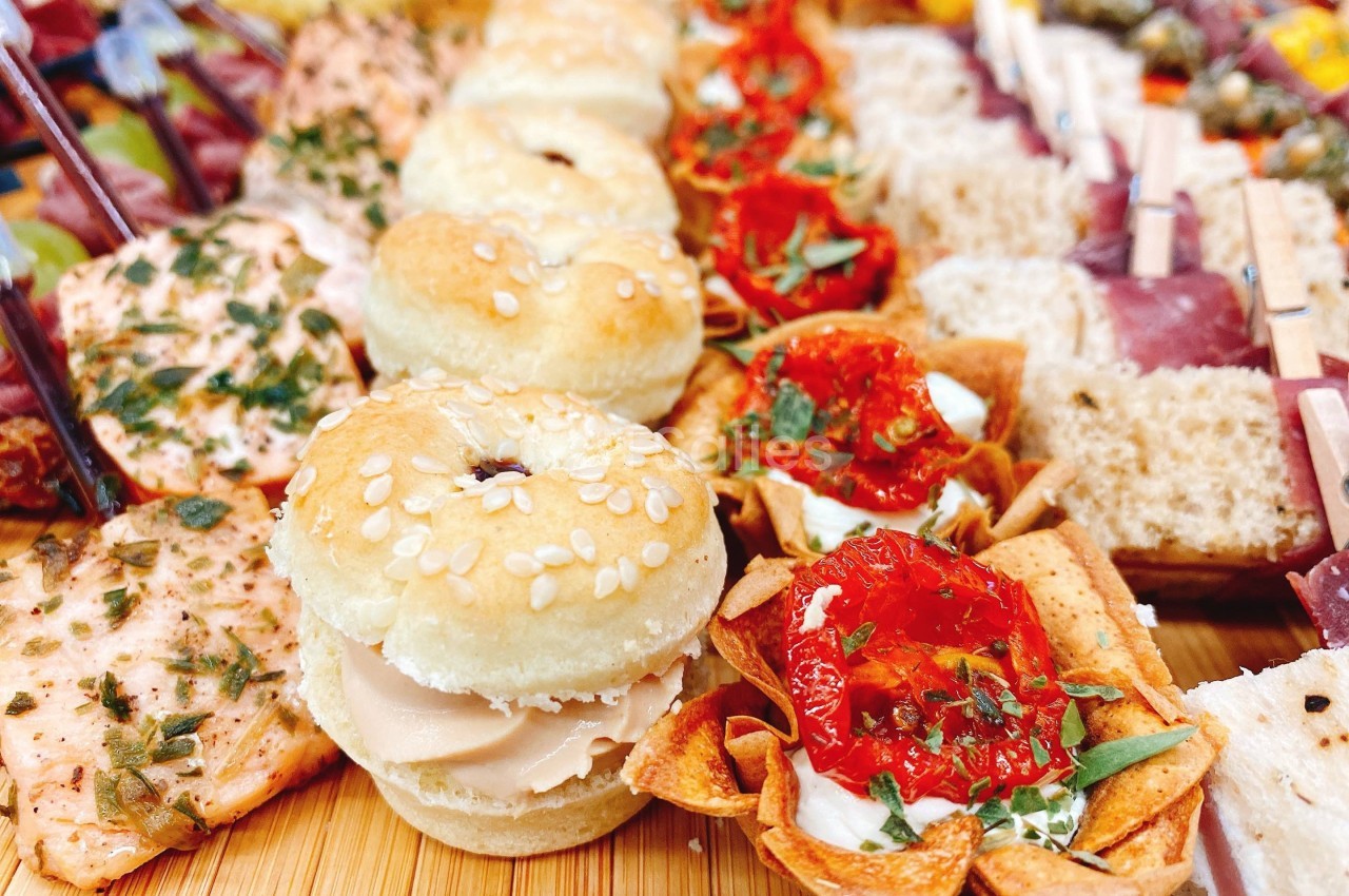 Plateau de bouchées variées comprenant mini-burgers, tartelettes aux tomates séchées et autres amuse-bouches.