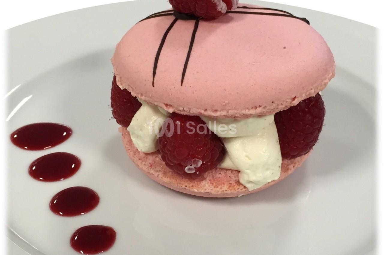 Macaron rose garni de framboises fraîches et de crème, décoré d'une framboise et de traits de chocolat, avec coulis.