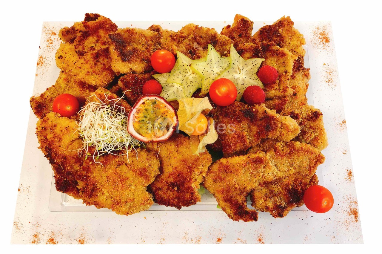 Assiette de filets panés garnie de fruits exotiques, tomates cerises et germes, présentée sur un plat blanc.