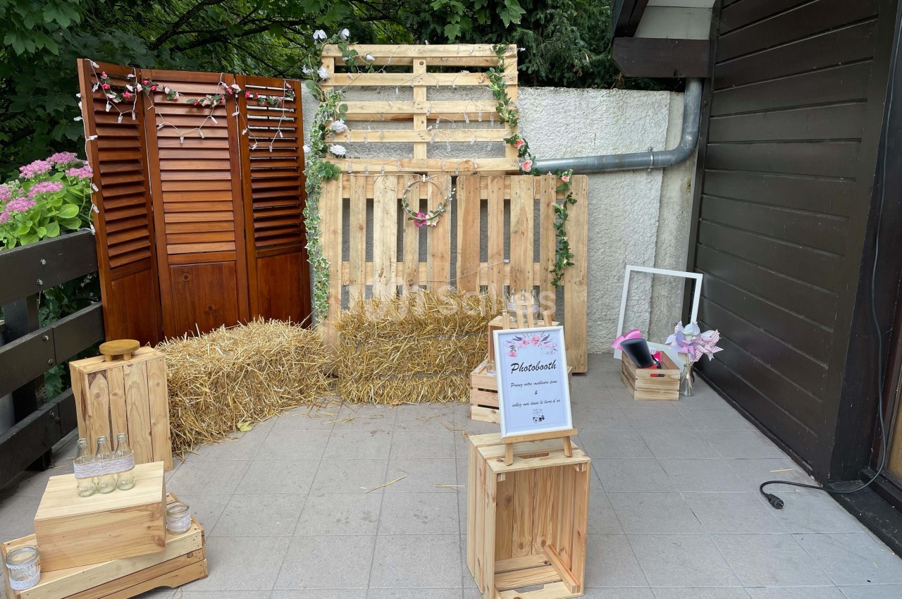 Décor champêtre avec palettes en bois, bottes de paille, guirlandes florales et caisses en bois sur une terrasse carrelée.