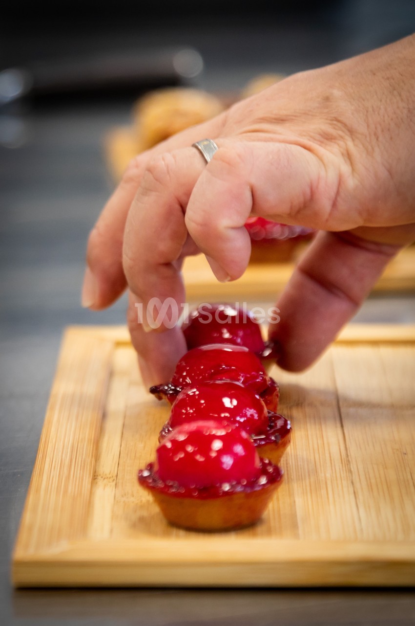 Main disposant des petites tartelettes garnies d'un glaçage rouge brillant sur une planche en bois.