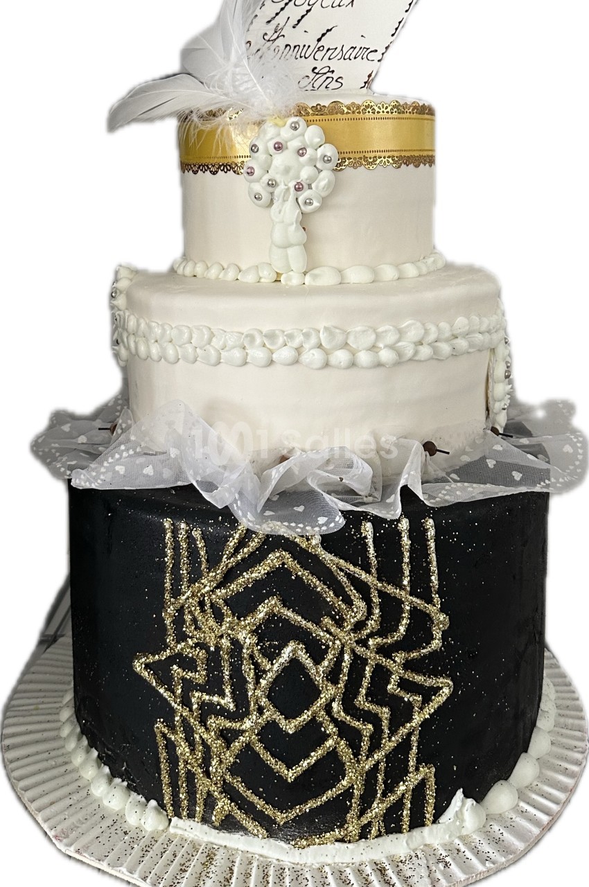 Gâteau à trois étages décoré de motifs dorés, plumes blanches et perles, avec une inscription d'anniversaire.