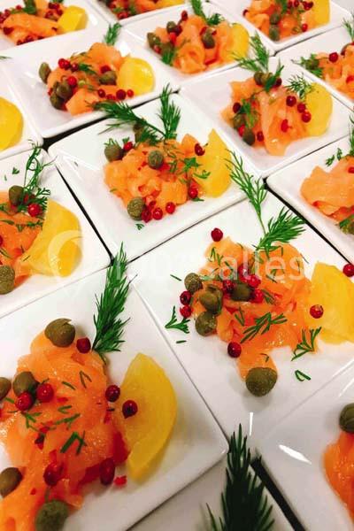 Assiettes individuelles de saumon fumé garnies de câpres, baies roses, aneth et quartiers de citron.