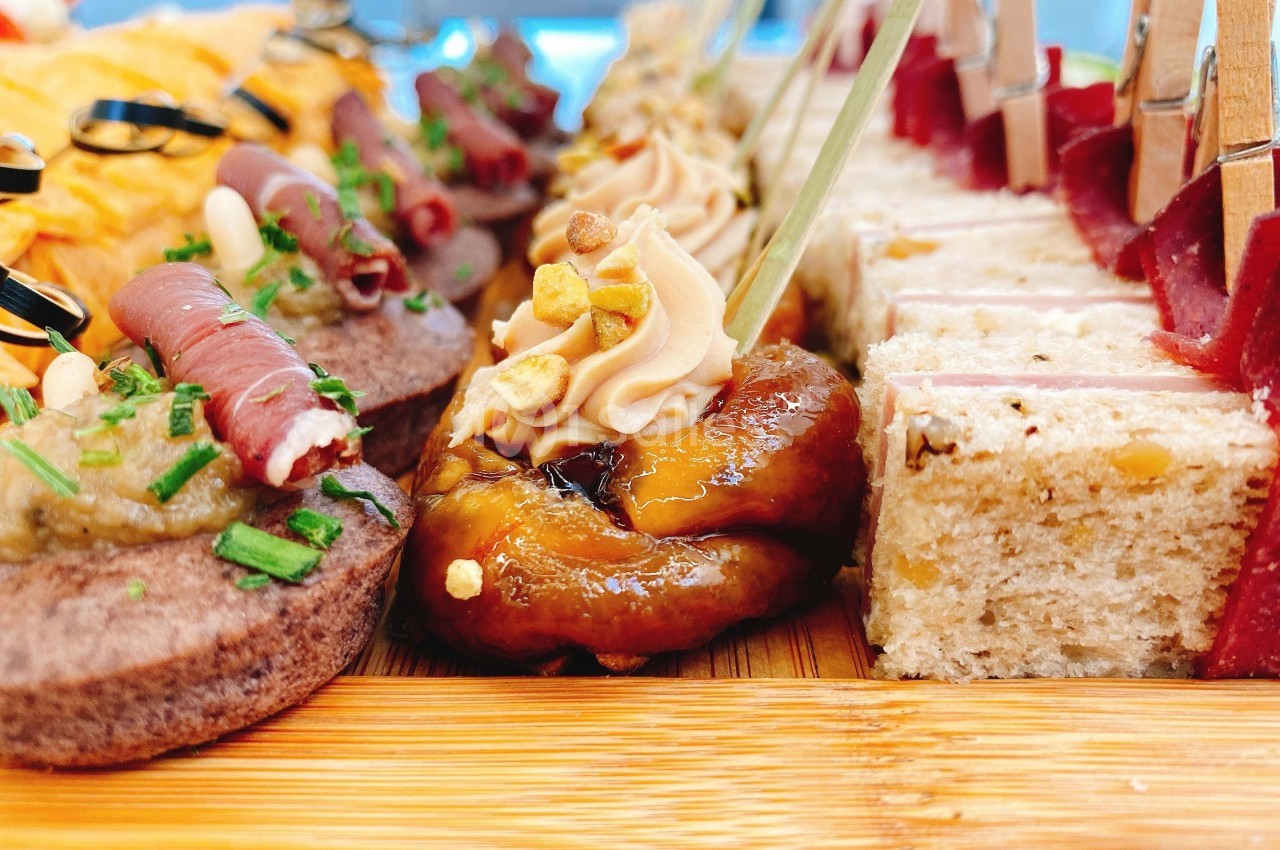 Assortiment de bouchées apéritives variées disposées sur un plateau en bois, incluant toasts, viandes et garnitures.