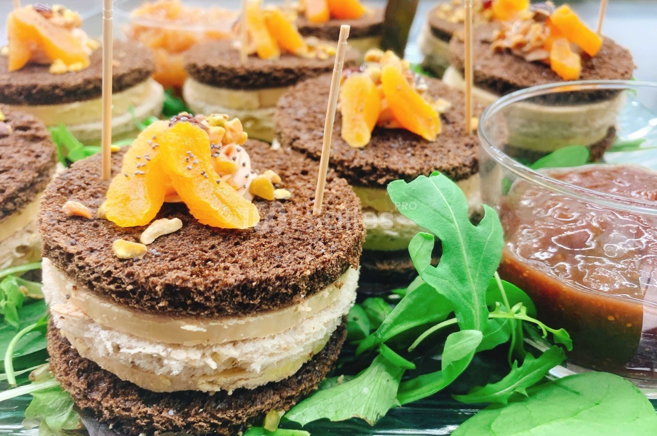 Canapés de pain noir garnis de foie gras, abricots secs et éclats de noisettes, servis sur un lit de roquette avec chutney.