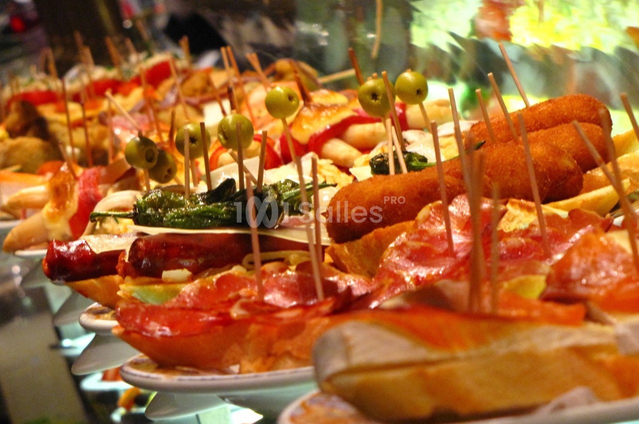 Assortiment de tapas variés présentés sur des assiettes, avec brochettes, olives, charcuterie et autres garnitures.
