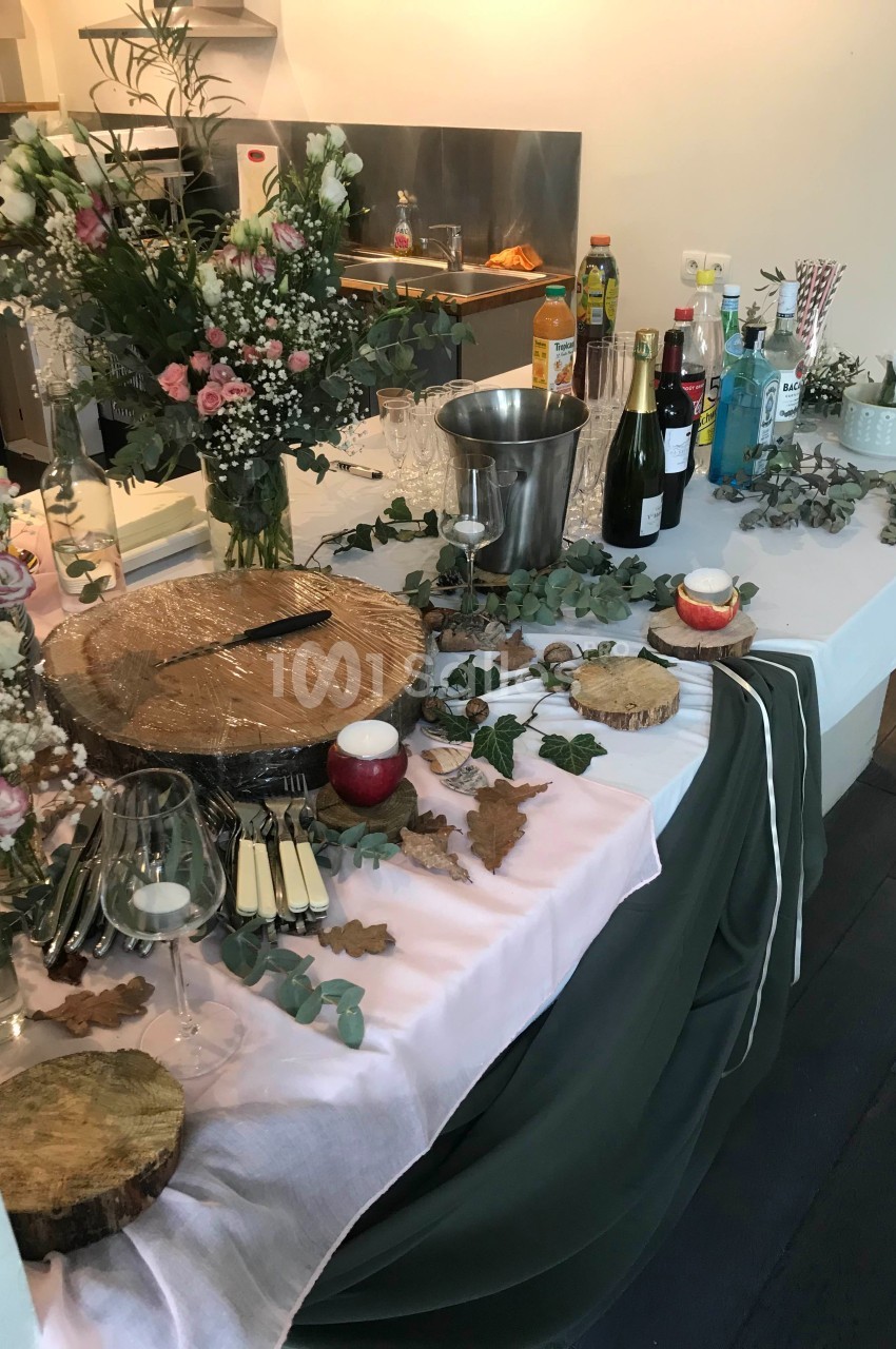 Table décorée pour un buffet avec fleurs, boissons, verres, planches en bois et couverts disposés.