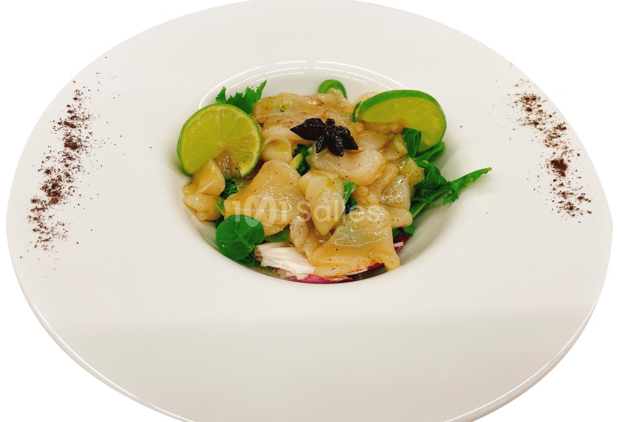 Assiette de carpaccio de Saint-Jacques avec tranches de citron vert, salade verte et décoration de poudre épicée.