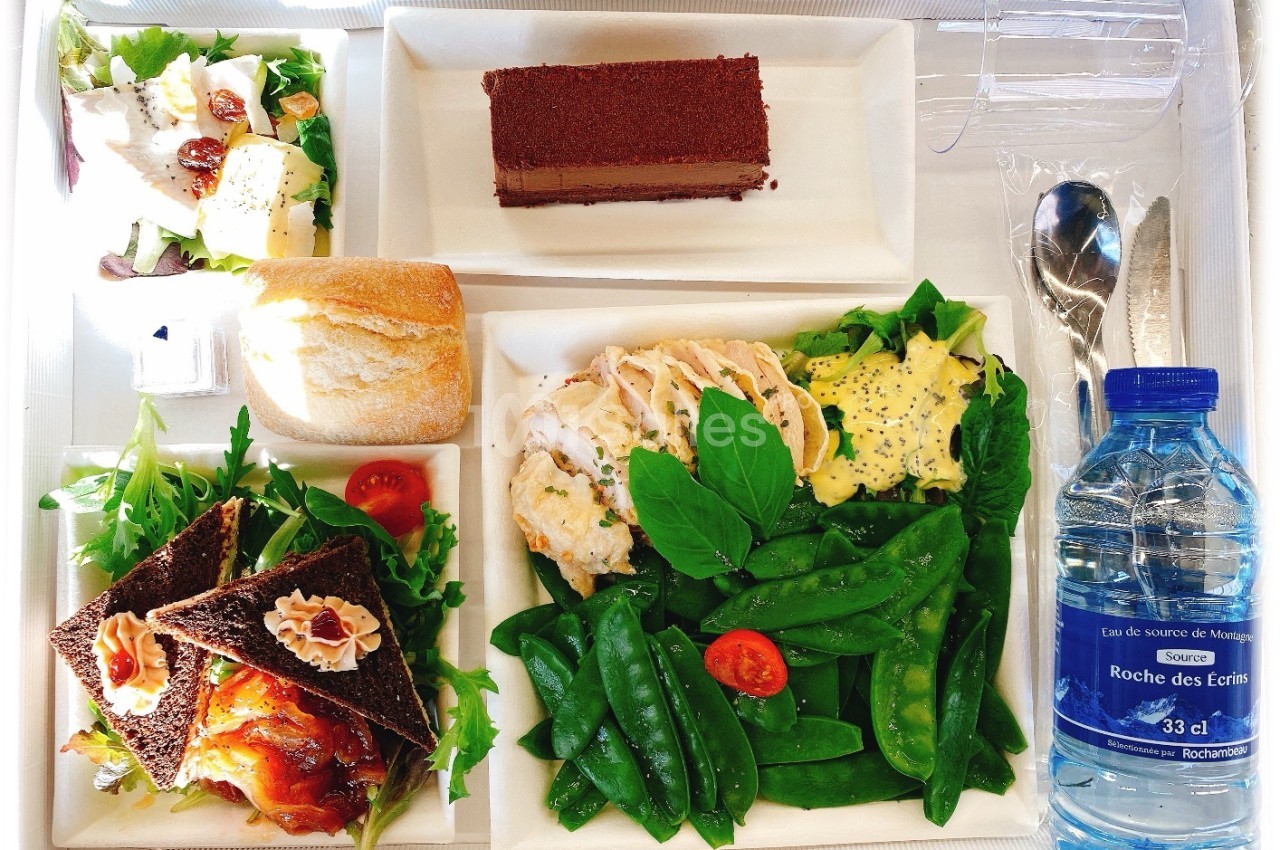 Plateau-repas avec salade, pain, sandwichs, poulet, légumes verts, dessert au chocolat et bouteille d'eau.