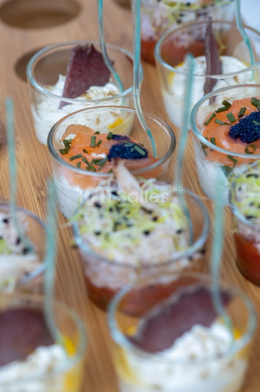 Verrines variées avec saumon, crème, herbes, œufs de poisson et garnitures, présentées sur un plateau en bois.