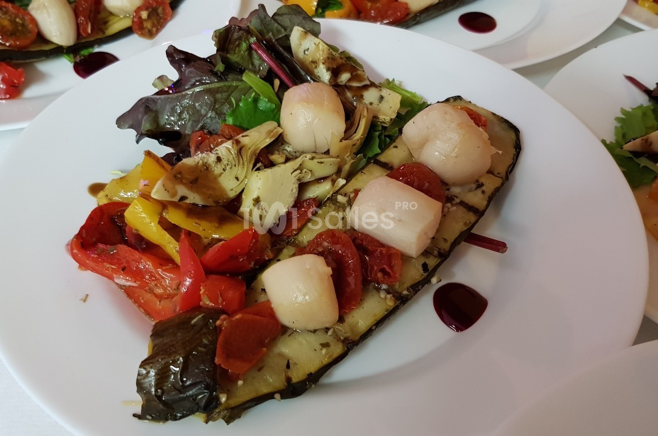 Assiette de légumes grillés avec noix de Saint-Jacques, accompagnée de salade et d'une sauce décorative.