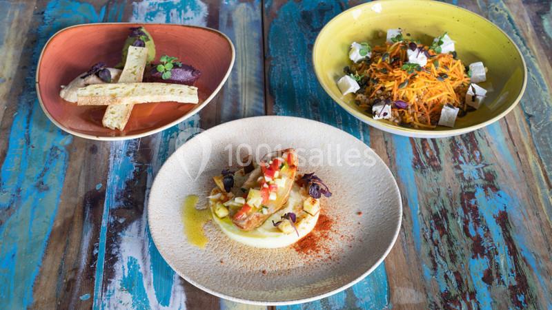 Trois assiettes de plats variés présentées sur une table en bois colorée, incluant légumes, pain et garnitures.