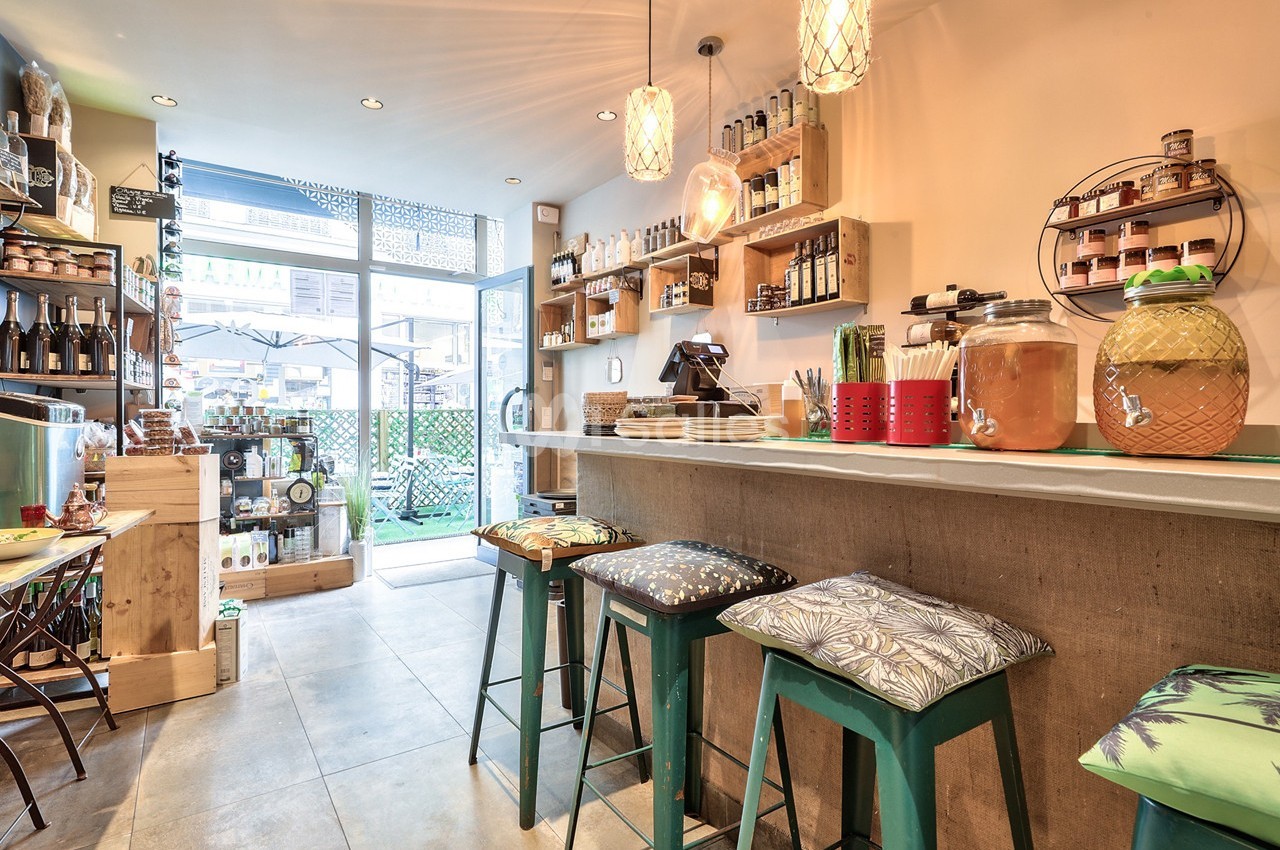 Intérieur d'un café chaleureux avec comptoir, tabourets colorés, étagères garnies de produits et vue sur l'extérieur.