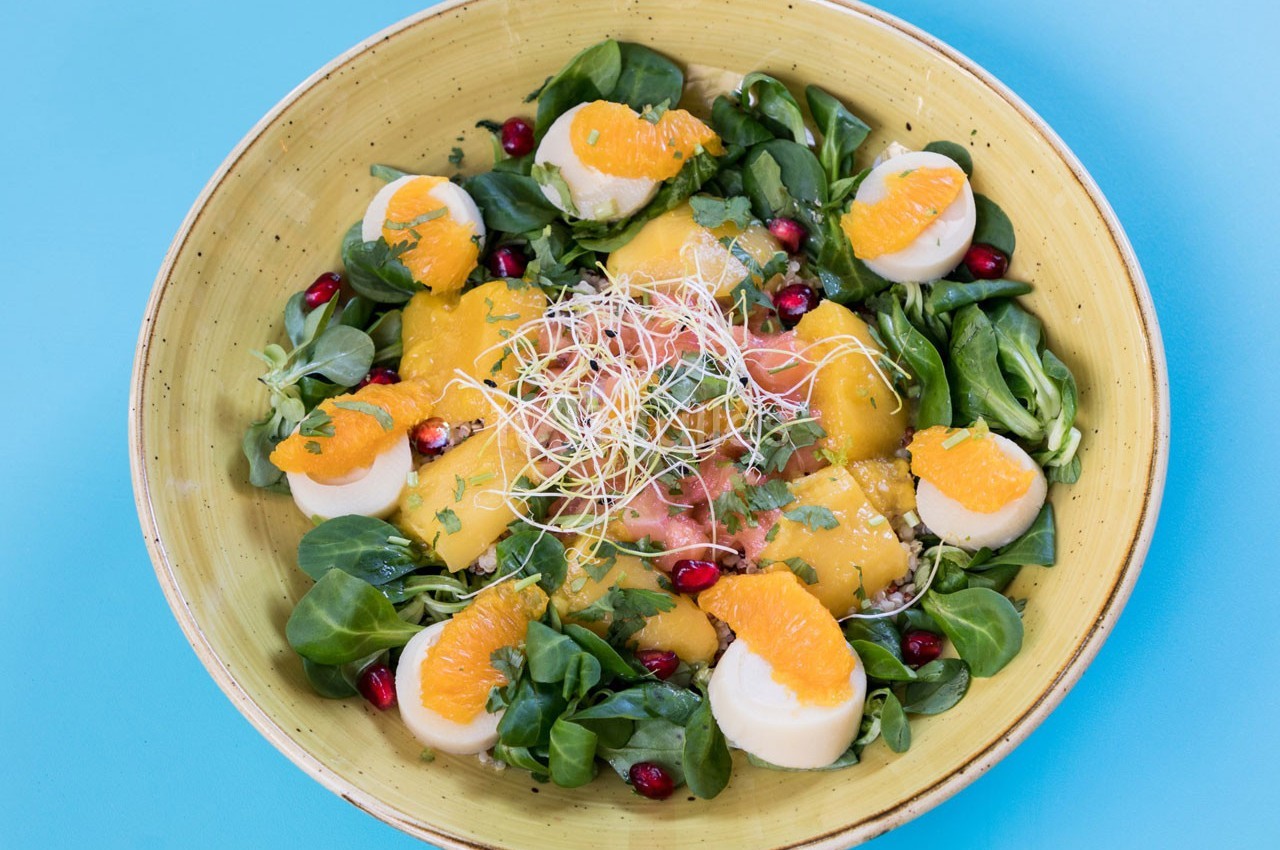 Salade colorée avec mâche, tranches d'orange, graines de grenade, fromage et germes sur une assiette jaune.