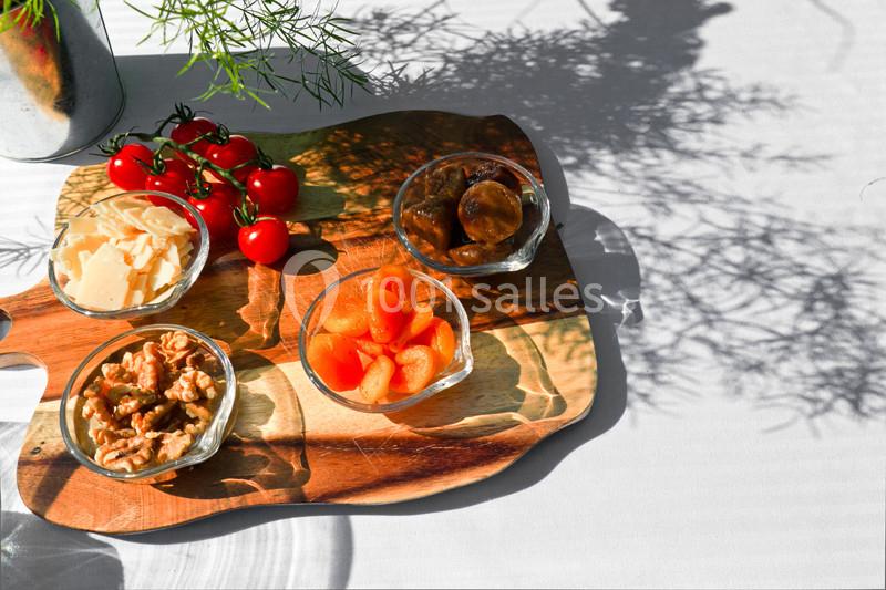 Planche en bois avec des bols contenant noix, tomates cerises, abricots secs, figues et copeaux de fromage, éclairée par le…
