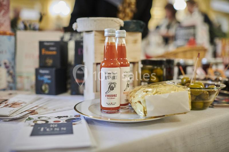 Bouteilles de sauce piquante sur une assiette avec olives, fromage et brochures, exposées sur une table lors d'un événement.