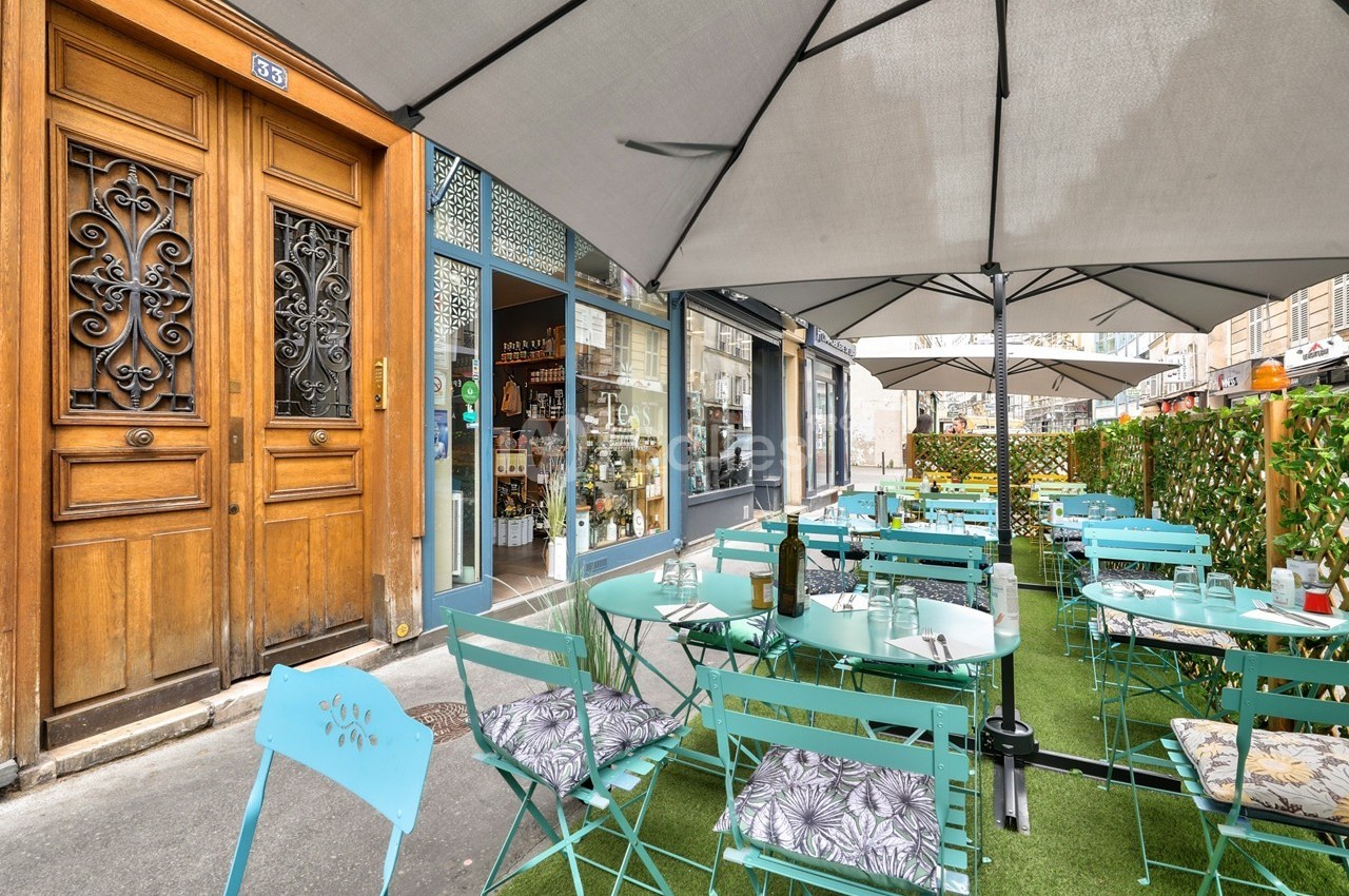 Terrasse extérieure avec tables et chaises turquoise, parasols, et vue sur une devanture de boutique en ville.