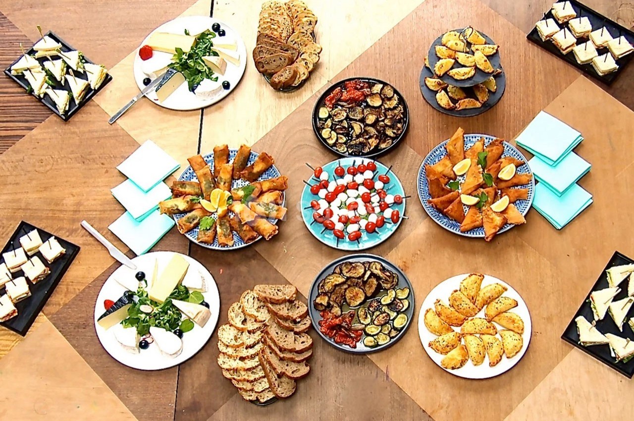 Assortiment de plats apéritifs variés disposés sur une table en bois, comprenant légumes, pains et amuse-bouches.