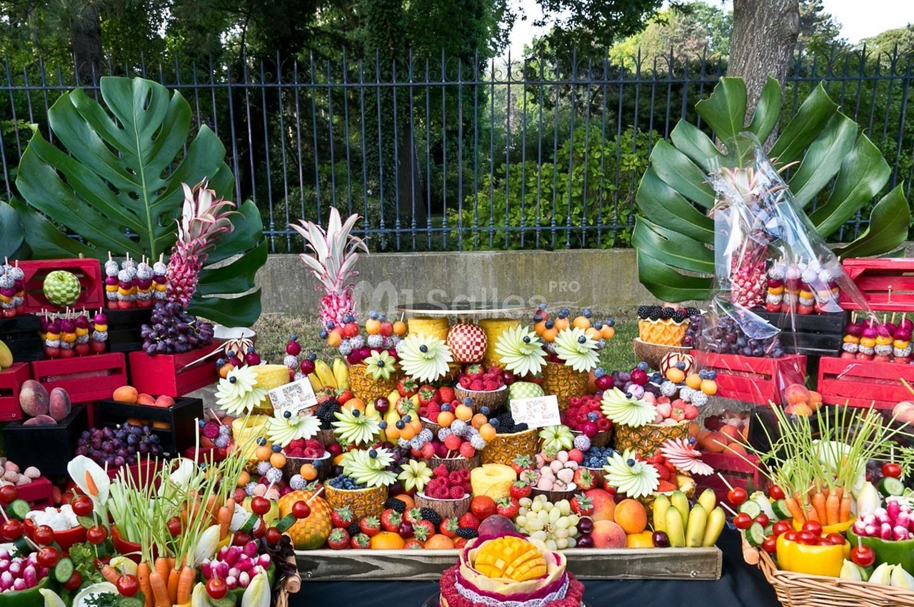 Présentation colorée de fruits variés et découpés, disposés sur une table avec des feuilles tropicales en arrière-plan.