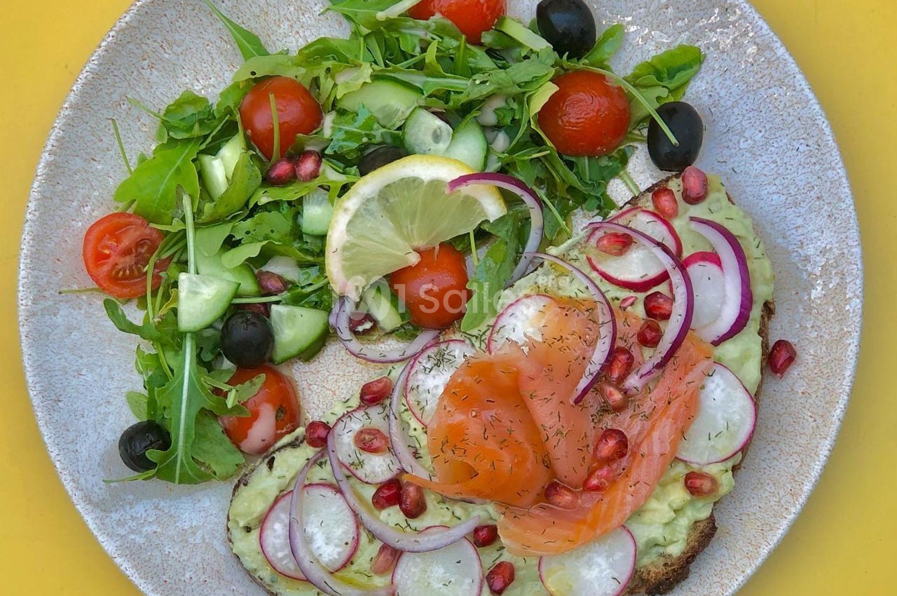 Assiette avec toast à l'avocat, saumon fumé, radis, grenade et salade verte garnie de tomates cerises et olives.