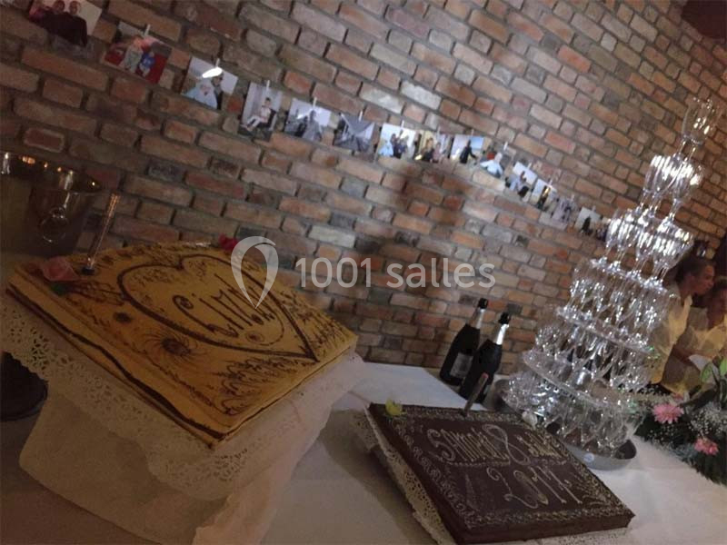Gâteaux décorés et pyramide de verres sur une table dans une salle en briques, avec photos suspendues au mur.