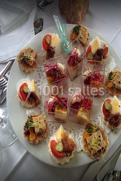 Assortiment de canapés et verrines colorés disposés sur un plateau rond, prêt à être servi.