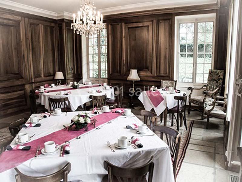 Salle à manger élégante avec tables dressées, nappes blanches et chemins de table roses, éclairée par un lustre et des…