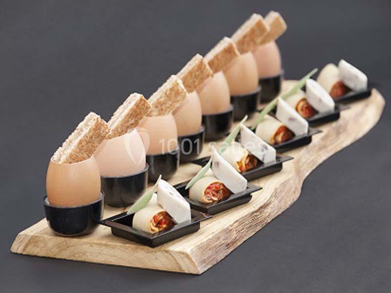 Œufs à la coque présentés avec des mouillettes et des amuse-bouches sur un plateau en bois.