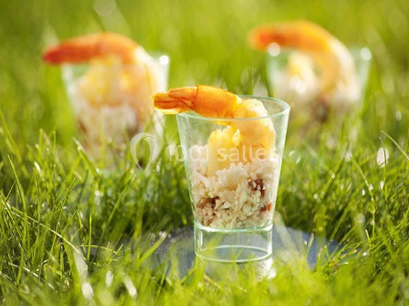 Verrines garnies de crevettes, riz et ananas, posées sur de l'herbe verte en extérieur.