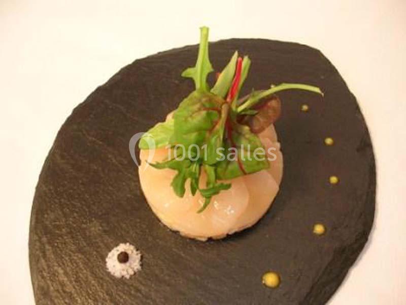 Plat dressé sur une assiette en ardoise, composé de carpaccio de Saint-Jacques, jeunes pousses et points de sauce.