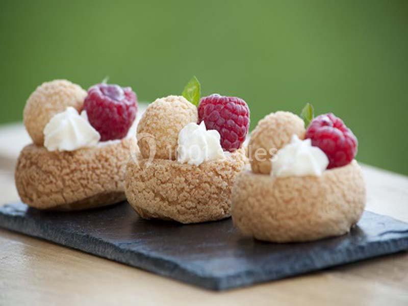 Pâtisseries individuelles garnies de crème, framboises et feuilles décoratives, présentées sur une ardoise.
