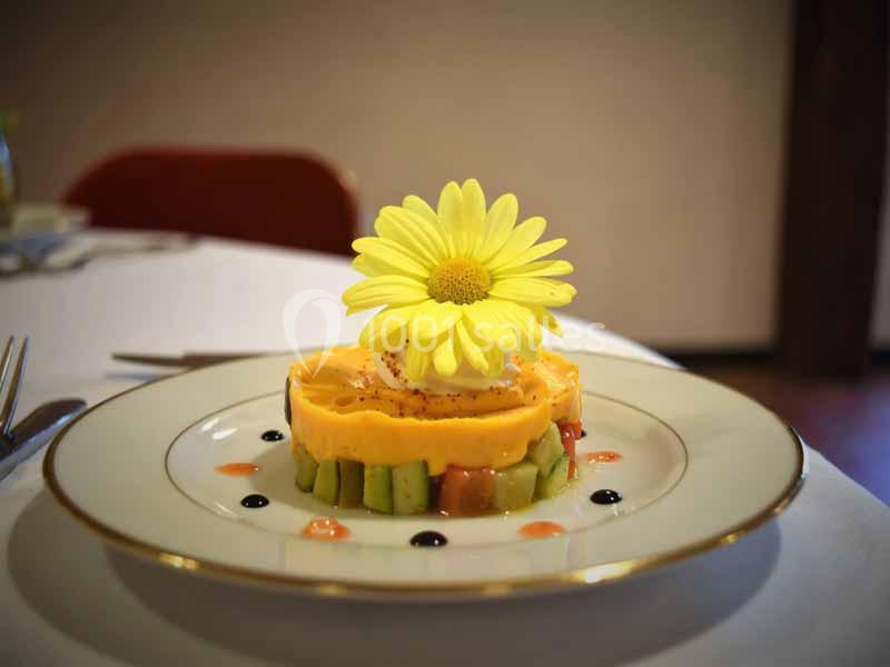 Dessert coloré avec une base d'avocat, une mousse orange et une fleur jaune en décoration, présenté sur une assiette.