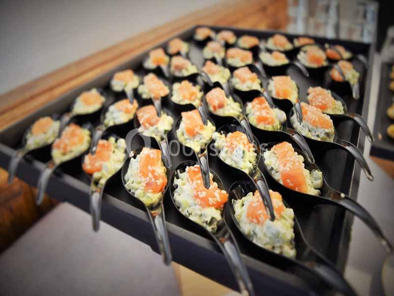 Cuillères apéritives garnies de tartare de saumon et d'une préparation crémeuse, disposées sur un plateau noir.